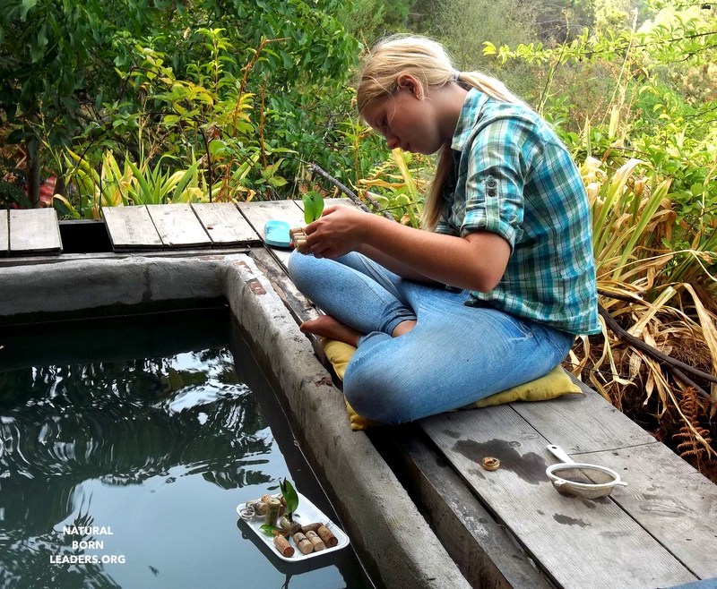 teenage girl making a cork boat and floating it in a water tank using natural resources - example of exploring natural gifts to support entrepreneurial spirit
