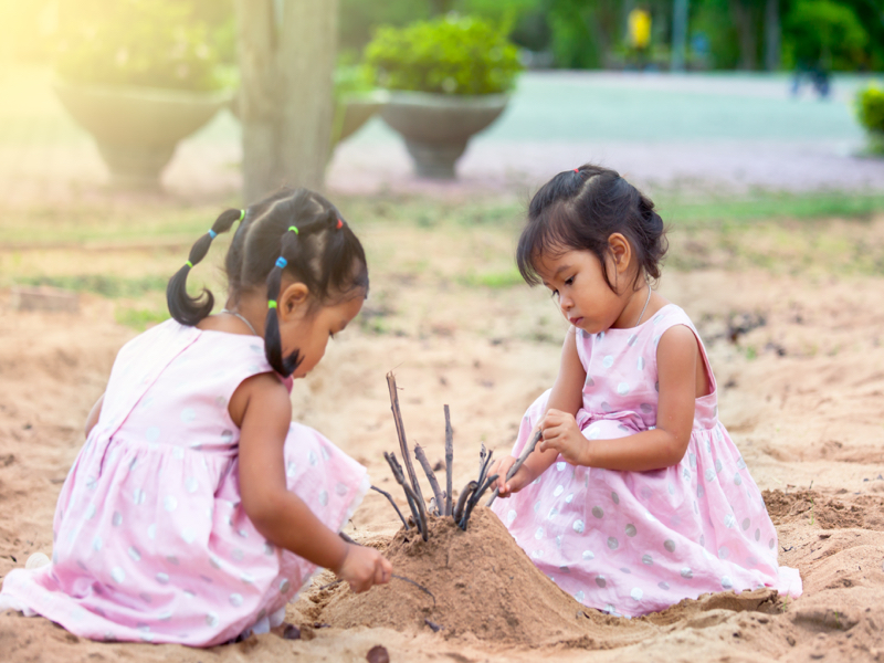 outdoor learning preschool girls building sand castle with sticks