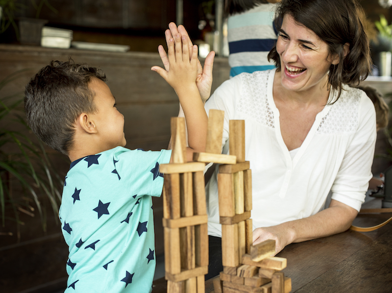 a woman/teacher building wooden blocks together and cheering for success - nurturing children's confidence 