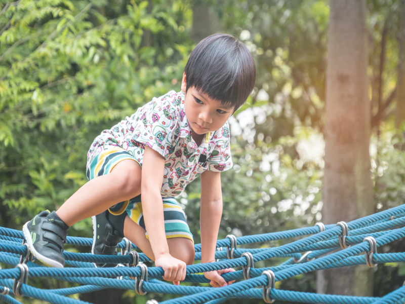 Preschool boy taking a manageable risk by climbing a net