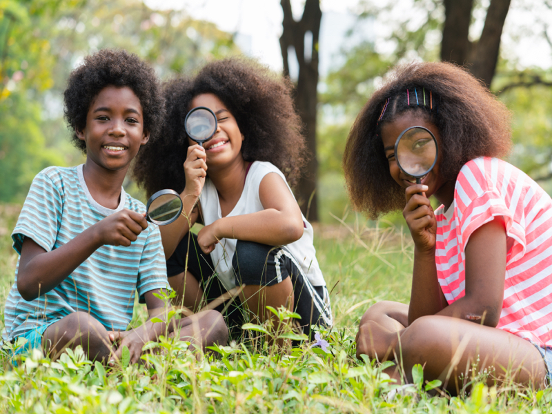 Primary school children engaged in outdoor experiential learning activities with magnifying glass