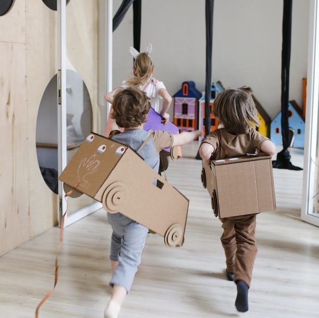 Preschool children engaged in role play running around the class wearing a cardboard made car toys