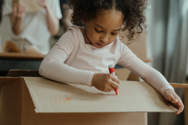 preschool girl writing on a cardboard box 